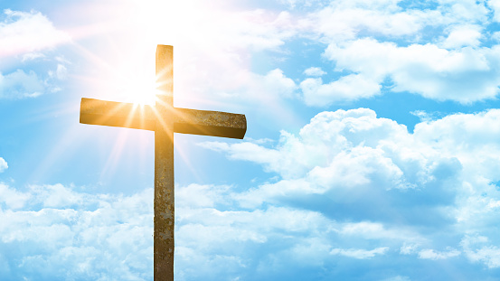 Fondo religioso - Antigua cruz de acero con cielo azul, nubes y rayos de sol photo