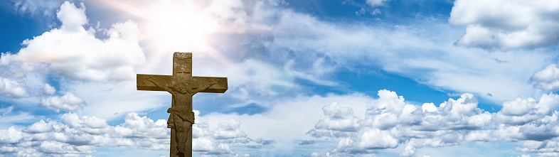 Religious crucifixion Easter background banner panorama - Old stone cross crucifix with blue sky, clouds and sunbeams