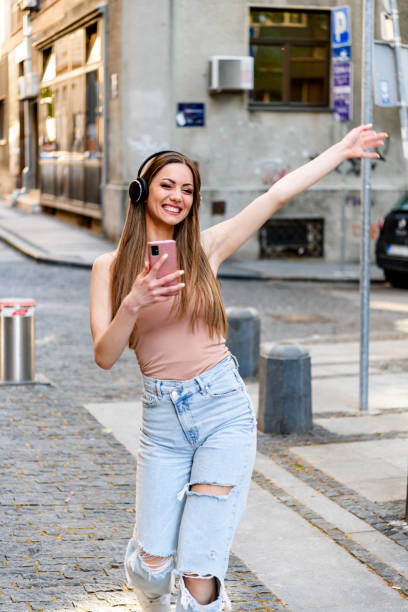 istock Young woman with smartphone dancing outdoors on street 1393343038
