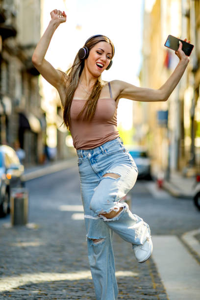 Excited girl dancing and listening music with headphones and smart phone in the street