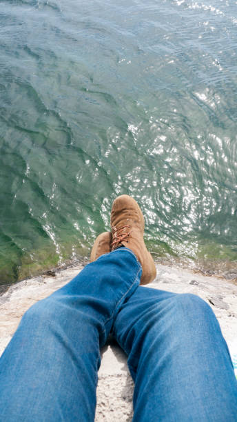istock Legs in jeans and boots hanging in a dock by a lake 1393344590