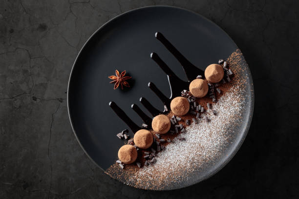 Chocolate truffles on a black plate with chocolate sauce.