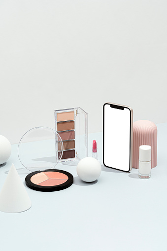 Blank screen smart phone mockup, template and cosmetics flat with geometric objects on white and gray background. Eye shadow, lipstick, nail polish, blusher, makeup palette with sphere, cone and geometric shape objects.