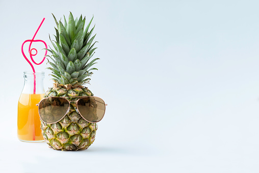 A bottle of fruit juice and a pineapple wearing sunglasses in front of white background.