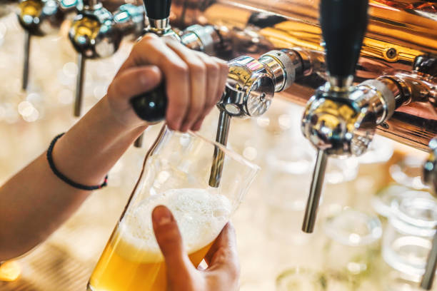 Woman bartender hand at beer tap pouring a draught beer in glass serving in a bar or pub stock photo
