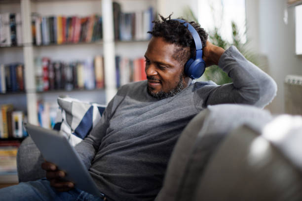 Smiling man with bluetooth headphones watching movie on digital tablet at home stock photo