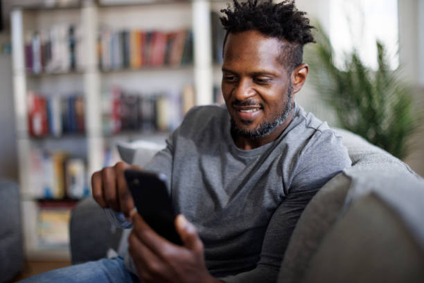 istock Smiling man sitting on couch and using phone 1393357107