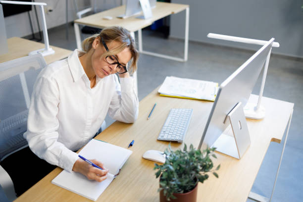 istock Tired female office worker writing in a notebook while sitting at the workplace 1393359350