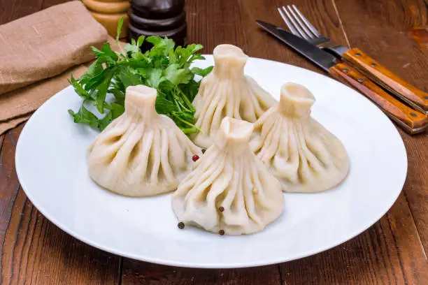 Photo of Khinkali with lamb on a white plate on wooden table