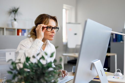 Una mujer de negocios bastante madura con gafas trabaja en una computadora en la oficina. Secretaria o contadora que trabaja en línea photo