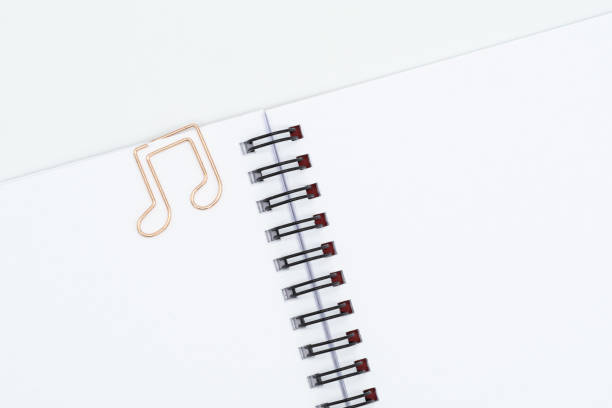 büroklammer in notenform auf spiralförmigem notizbuch auf weißem hintergrund - note pad paper spiral diary stock-fotos und bilder