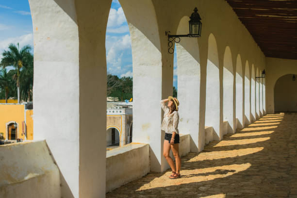 frau geht zwischen säulen in der stadt izamal in mexiko spazieren - women rear view one person arch stock-fotos und bilder