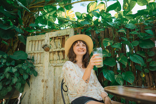 Young Caucasian woman  in straw hat drinking lemonade on backyard