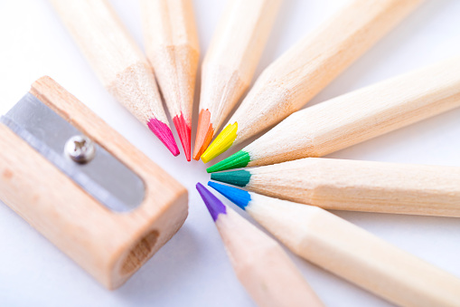 Top view of various wooden colored pencils arranged side by side on a semicircle shape beside a wooden sharpener on white background