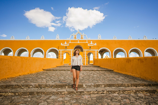 Young Caucasian woman in straw hat  walking in yellow Izamal town in Mexico, Yucatan