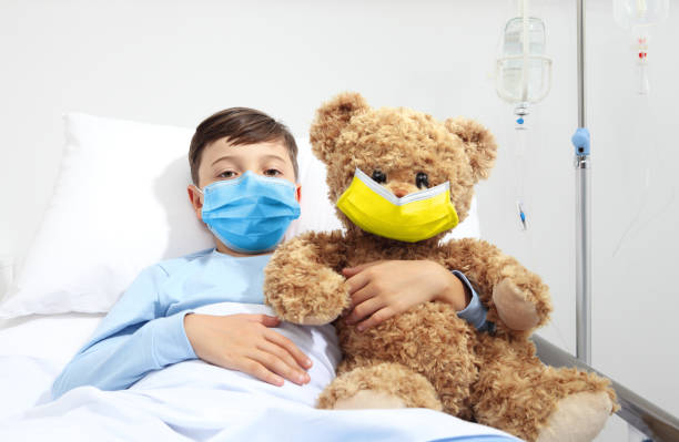 ayuda humanitaria, ayuda para la protección médica para la guerra de ucrania, niño en cama de hospital con oso de peluche con máscara facial protectora de colores amarillo y azul de la bandera de ucrania. refugiados ucranianos heridos - child physical injury teddy bear wound fotografías e imágenes de stock