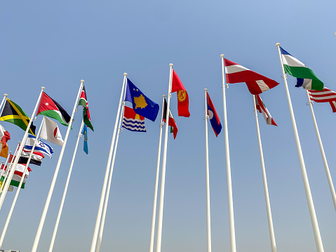 Looking up to Many world flags flying in a row outside of expo center in 2020 waving on blue sky background.