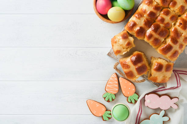 istock Easter hot cross buns with colored eggs, Easter gingerbread rabbits and cookies over white plank wooden old table background . Spring holiday baking concept. Easter table setting. Top view. Mock up. 1393377702