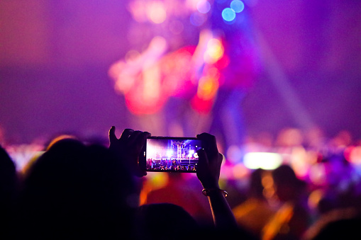 The picture of someone from crowd taking video of a live stage performance using his mobile. The picture was taken for a open air concert during the festival of Holi.