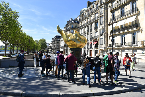 Paris, France-04 17 2022: People around the Flame of Liberty located Place Diana.\nThe Place Diana is a public square situated in the 16th arrondissement of Paris, near the Seine river.The Flame of Liberty in Paris is a full-sized, gold-leaf-covered replica of the flame of the torch from the Statue of Liberty, located at the entrance to the harbor of New York City since 1886.\nSomewhat forgotten, the Flame benefited from a renewed interest when Diana, Princess of Wales died on August 31, 1997 during a road accident in the tunnel of pont de Alma, located below the monument.