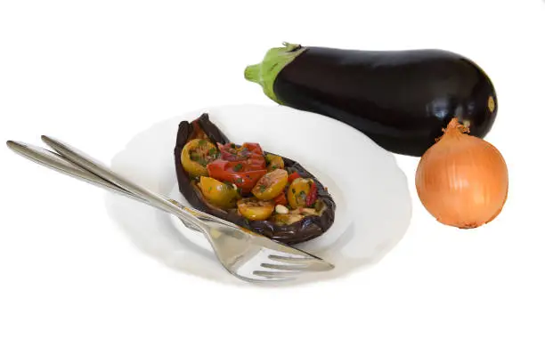 Photo of Eggplant baked with Italian tomatoes and pine nuts on white plate and fork with knife