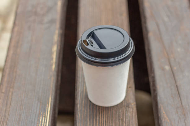 A paper cup of coffee is on a park bench
