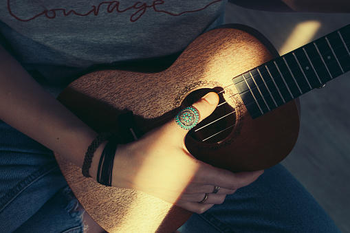 Hands with rings playing small guitar ukulele. Musical instrument. Vintage style.