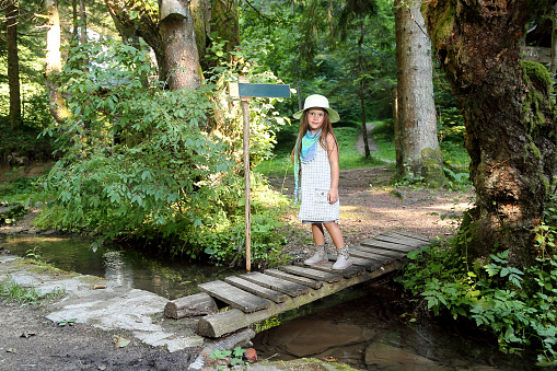 Beautiful little girl with a smile on her face stands on a forest bridge in the woods