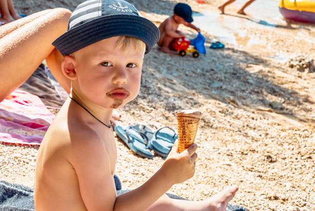 istock Cute little boy in hat eats ice cream sitting on beach 1393399016