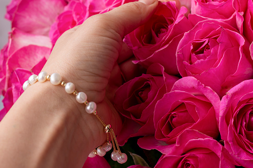 Buds of pink roses and a woman's hand with a pearl bracelet