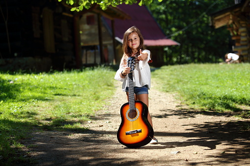 Little beautiful girl with a guitar in her hand poses and enjoys a summer day in nature