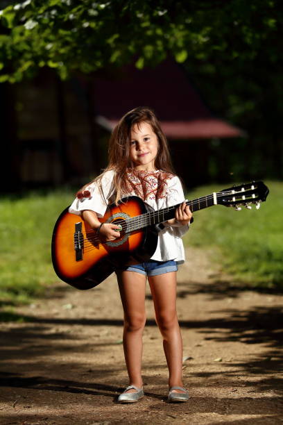 Little beautiful girl with a guitar in her hand poses and enjoys a summer day in nature