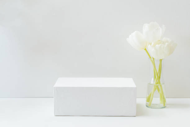 istock Geometric podium or pedestal with white spring tulips in a vase on a white background. Empty podium for product presentation 1393412034