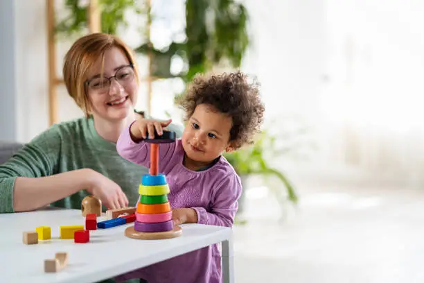 Photo of Mother looking at a child playing with an educational didactic toy