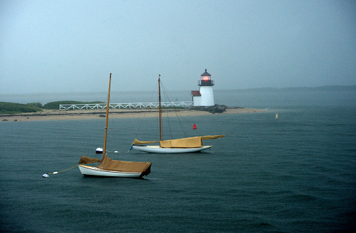 Beach side of Brant Point Lighthouse and sail boats along the harbor of the sea waters of the Atlantic ocean in Nantucket, Massachusetts.