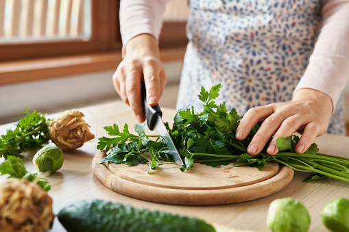 Woman preparing lunch - chopping fresh parsley, with green vegetables in the foreground