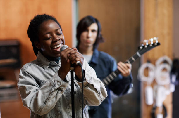 Young Woman Singing with Band in Studio Waist up portrait of young black woman singing to microphone while rehearsing with band in professional recording studio african musical instrument stock pictures, royalty-free photos & images