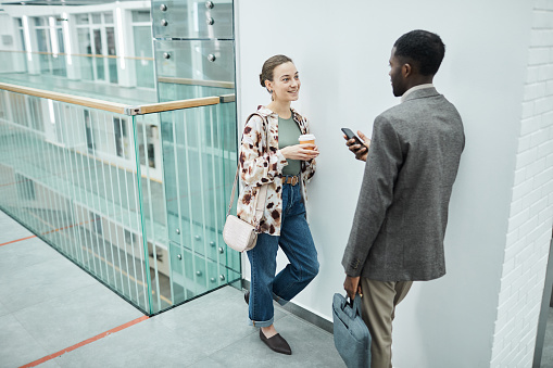 High angle portrait of two coworkers chatting at balcony in office building with modern architectural design, copy space