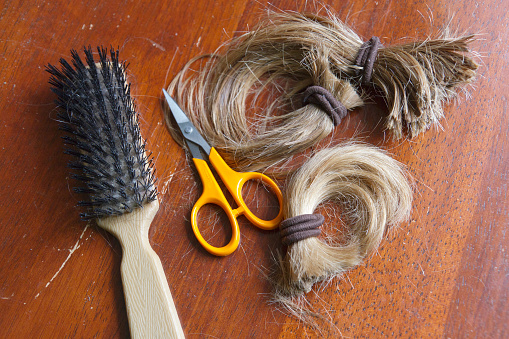 Close up of a thick, cut-off ponytail of long blond hair held together with brown hair ties along with a brush and scissors, indicative of a life change