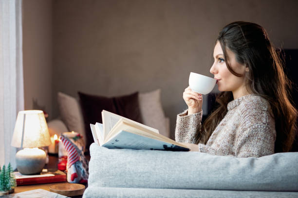 istock Young woman is drinking coffee and reading book on the sofa 1393430067