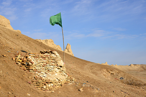 Balkh / Vazirabad, Balkh province, Afghanistan: green Islamic flag on the walls of the capital of ancient Bactria, Ancient Balkh archeological site - ruined walled city enclosure - Greek-Kusahn city wall topped by Timurid wall, the former is melting into nature and the latter is mostly ruined - known as Bala Hissar ('High Fort') -  situated to the north of the modern city