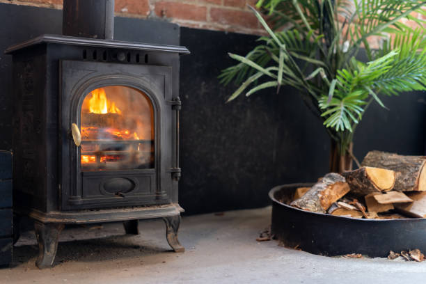 居心地の良いリビングルームの黒い金属製の暖炉の近くの薪 - burner ストックフォトと画像