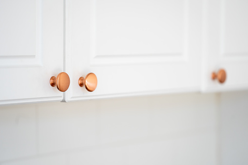 Round copper door handles on a white cabinet in a classic style