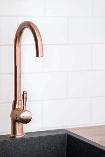 A close-up of a shiny, gold-colored kitchen faucet in a kitchen, captured in a 16:9 aspect ratio. The faucet and surrounding surfaces reflect the warm light, giving the image a luxurious and inviting atmosphere. The faucet is made of high-quality material, showcasing excellent craftsmanship and design. This image is ideal for topics such as kitchen equipment, cleanliness, and luxurious home design.