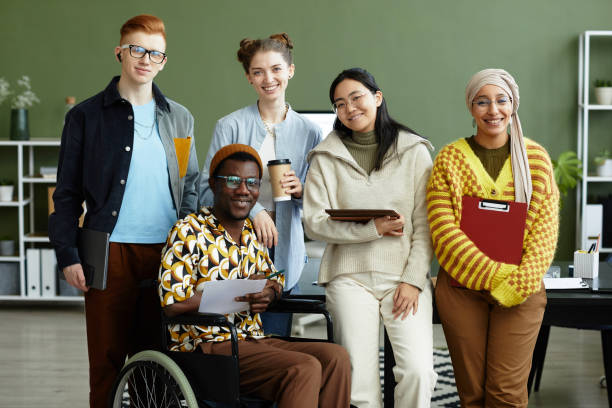 Diverse Business Team Portrait Portrait of diverse creative team looking at camera with cheerful smiles while posing in office, wheelchair user inclusion accessibility for persons with disabilities stock pictures, royalty-free photos & images