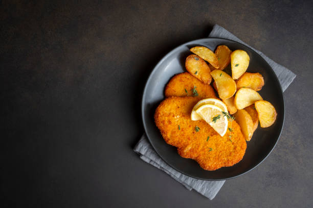 chicken schnitzel with sauce, fried potatoes and lemon in a plate - milanese imagens e fotografias de stock