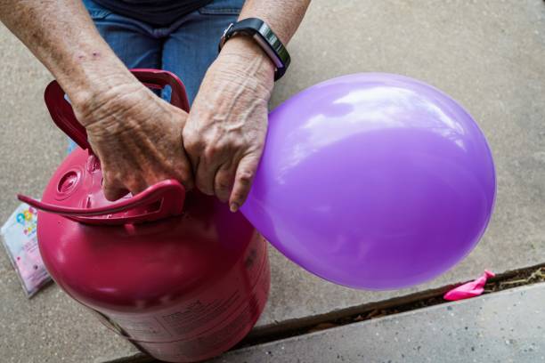 Senior Woman's hands Inflate Helium Balloons, Close-up Close-up of a senior woman's hands fills a purple balloon with helium gas from a tank for a special occasion. helium stock pictures, royalty-free photos & images