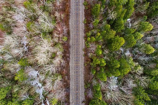 An aerial drone view of a railroad line through forest in Spring, some snow still visible.