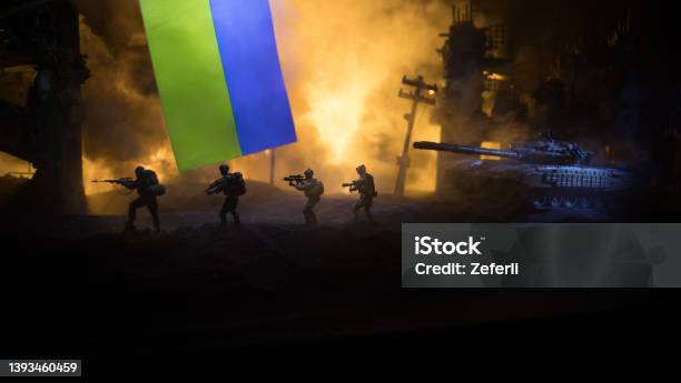 Russian War In Ukraine Concept Silhouette Of Armed Soldiers Against Ukrainian Flag And Burned Out City Creative Artwork Decoration Night Fighting Scene Stock Photo - Download Image Now