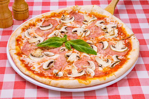 Pizza with ham and mushrooms on plate on red italian table